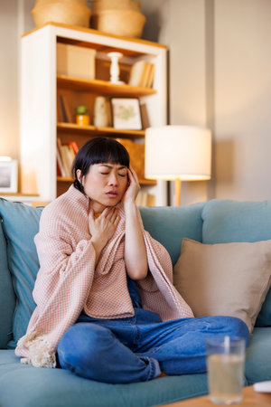 Sick woman having fever and headache covered with blanket relaxing at home while on sick leaveの写真素材