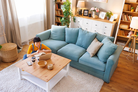 High angle view of mature Asian woman taking an online educational course class using laptop computer, taking notes in a plannerの写真素材