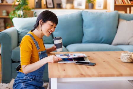 Mature Asian woman relaxing at home reading magazine and drinking coffeeの写真素材