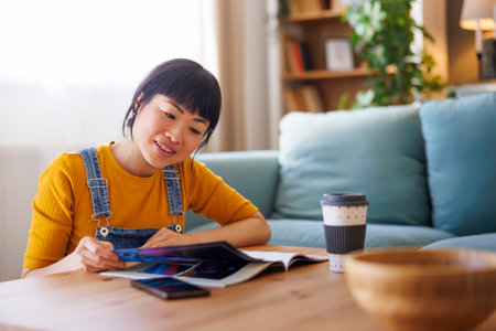 Mature Asian woman relaxing at home reading magazine and drinking coffeeの写真素材