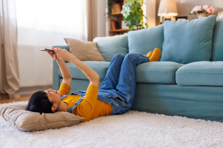 Mature Asian woman using smart phone while relaxing and enjoying leisure time at homeの写真素材