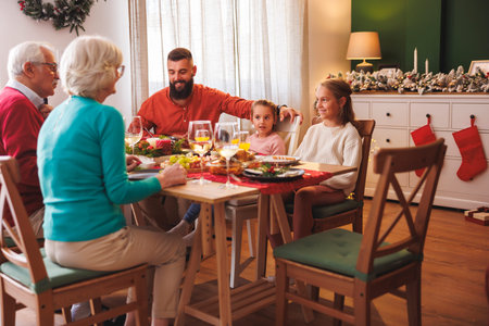Happy multi-generation family gathered around the table, having Christmas dinner all together at...