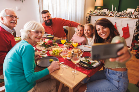 Multi-generation family gathered at home for Christmas dinner having fun taking selfies and enjoying...