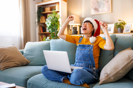 Cheerful Japanese woman wearing Santa hat having video call with friends and family using laptop computer while celebrating Christmas at homeの写真素材