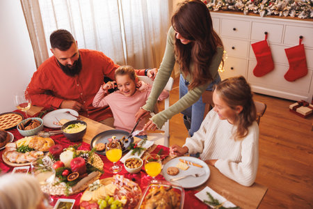 Happy family gathered around the table while having Christmas dinner all together at homeの写真素材