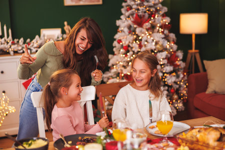 Happy family gathered around the table having Christmas dinner all together at home, mother and daughters having fun singing Christmas songsの写真素材