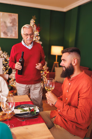 Senior man opening a bottle of wine while having Christmas dinner with family at homeの写真素材