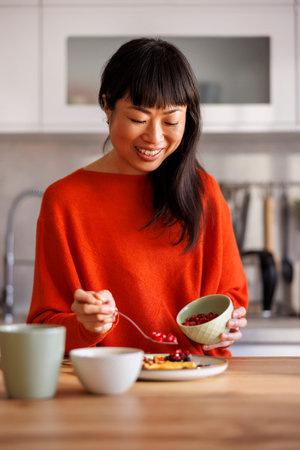Beautiful young woman having waffles with fresh berries and caramel topping for breakfast, enjoying...
