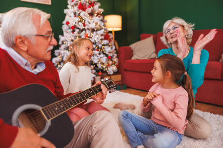 Grandparents having fun spending Christmas day with granddaughters at home, sitting by the Christmas...