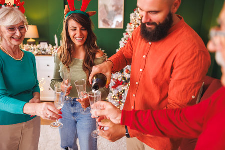 Adult children having fun spending winter holiday season with senior parents at home, opening a bottle of champagne while celebrating Christmasの写真素材