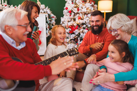 Happy multi-generation family having fun playing the guitar and singing Christmas songs while spending Christmas day all together at homeの写真素材