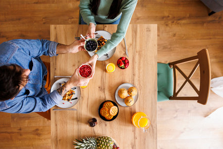 Top view of beautiful couple in love passing food to each other while having breakfast at home, relaxing and enjoying their leisure time togetherの写真素材