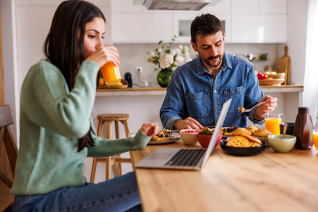 Beautiful couple having breakfast at home, woman working using laptop computerの写真素材