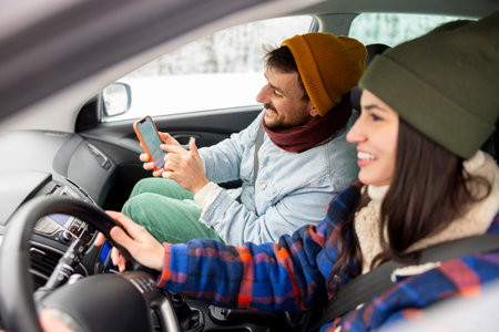 Cheerful couple in love having fun driving a car while travelling to a winter vacation road trip, using smart phone gpsの写真素材