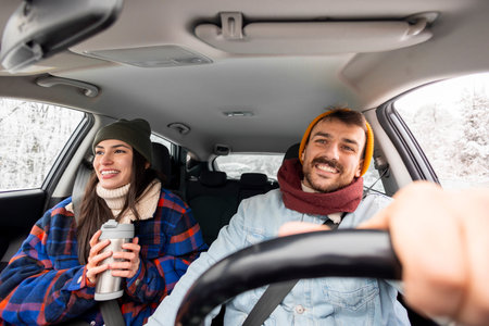 Cheerful couple in love having fun driving a car while travelling to a winter vacation road trip