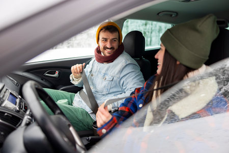 Cheerful couple in love fastening car seat belts , getting ready for travelling to a winter vacation...