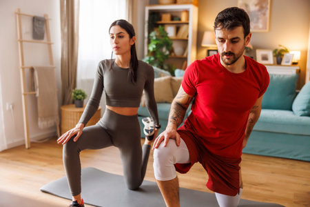 Active fit couple in sportswear doing leg stretching out while exercising together at home