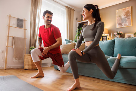 Active fit young couple in sportswear doing Bulgarian lunges or split squats, lower body exercise...