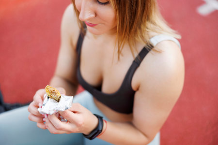 High angle view of young woman in sportswear sitting on an outdoor basketball court eating while taking workout breakの写真素材