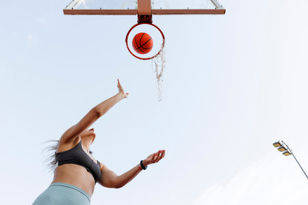 Low angle view of young woman in sportswear shooting hoops playing basketball as morning workout routineの写真素材