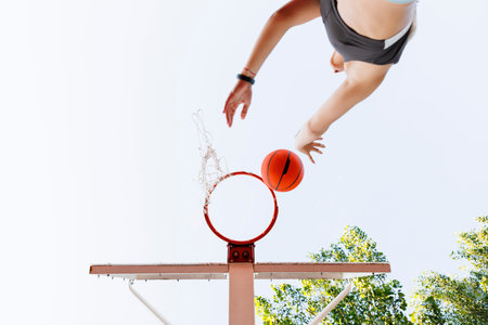 Low angle view of young woman in sportswear shooting hoops playing basketball as morning workout routineの写真素材