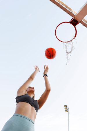 Low angle view of young woman in sportswear shooting hoops playing basketball as morning workout routineの写真素材