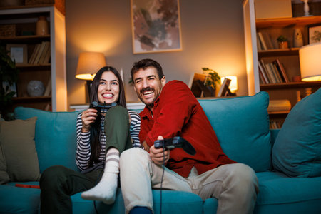 Beautiful young couple in love having fun playing video games while relaxing at home at night