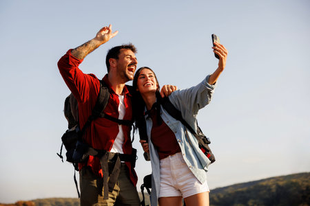 Active couple carrying backpacks having fun hiking in nature on sunny summer day, taking a break...