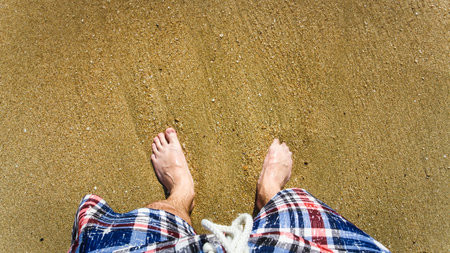 Top view of man's legs in shorts on sand in sunlight
