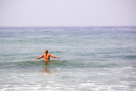Beautiful woman walks into calm water. Photo from the backの写真素材
