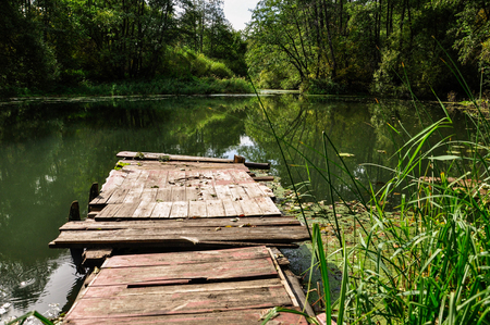 Wooden platform for fishing on the river in summer. Reflection of trees and sky in the water.の写真素材