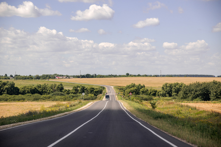 Empty asphalt road through two green field and clouds on blue sky in summer dayの写真素材