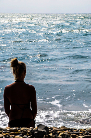 silhouette of young woman sitting back alone on a rock at the beachの写真素材