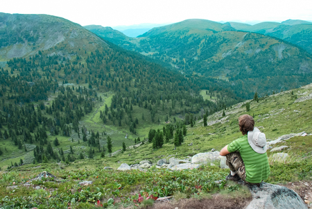 Young caucasian white man sitting on rock and enjoying scenic view at a mountain landscape in Siberiaの写真素材