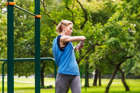 Young attractive sporty girl smart watch pulse meter and warming up before training in park. Stretching handsの写真素材