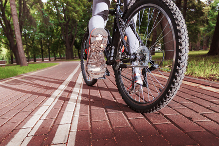 Close-up view on a cyclist on the road. Biker riding a bike on the way view from below on a background of green parkの写真素材