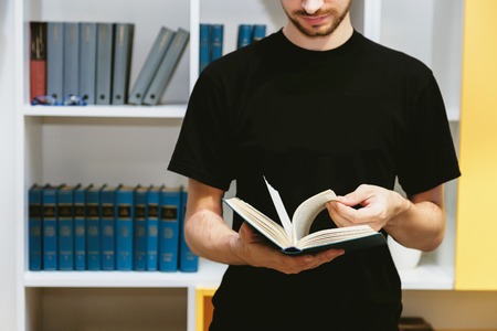 Man reading. Book in his hands. Bookshelf in the backgroundの写真素材