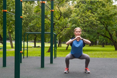 Beautiful girl doing squats outdoor sport siteの写真素材