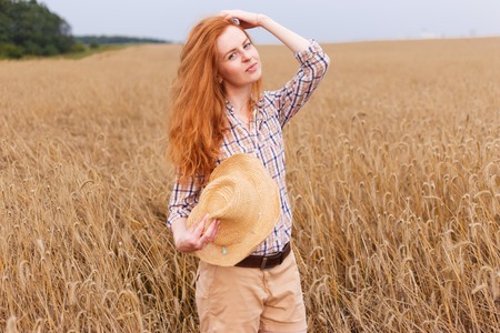 Young red hair beautiful woman in golden wheat fieldの写真素材