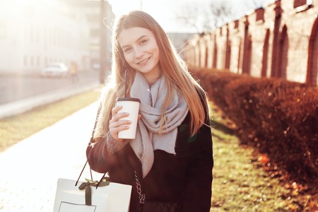 Beautiful girl with shopping bag holding cup of warm drink.の写真素材