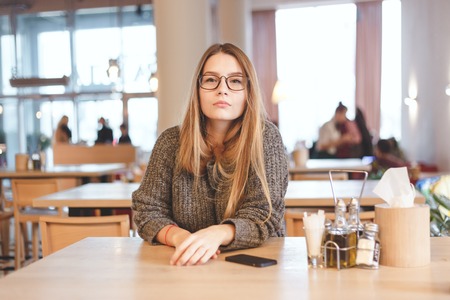 Portrait of cute freelancer girl sitting in a cafe. She wears brown hipster eyeglassesの写真素材