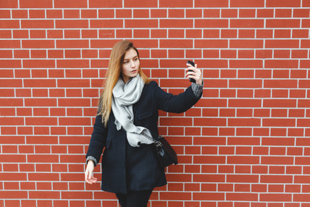 Outdoor portrait of pretty student girl taking a selfie on mobile phone. Autumn