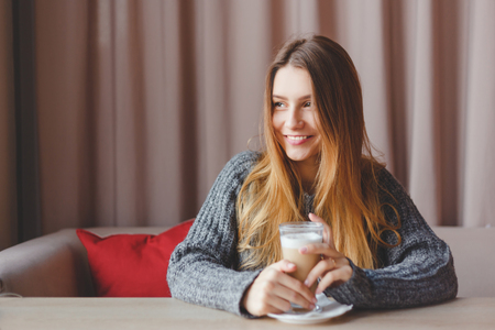 Gorgeous winter girl in knitted sweater dreams with a cup of hot coffeeの写真素材