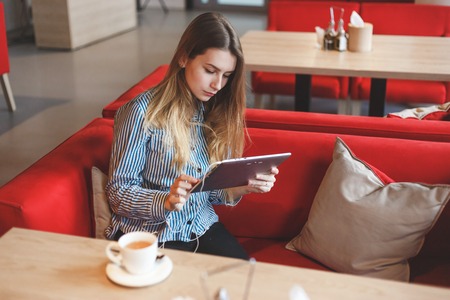 Beautiful girl in a cafe with tablet and cup of teaの写真素材