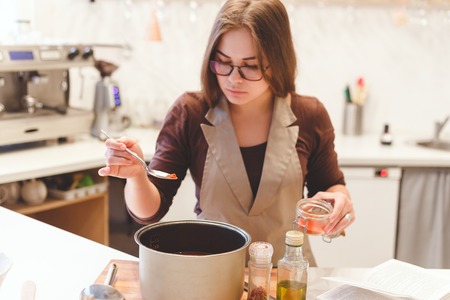 Happy female adds salt or spices into soup pan at her kitchenの写真素材
