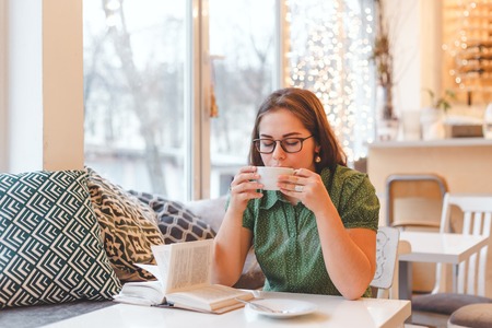 Portrait of young gorgeous female drinking tea and thoughtfully looking out of the coffee shop window while enjoying her leisure time alone, nice business woman lunch in cafe during her work breakの写真素材