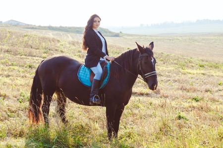 Gorgeous brunette girl wearing fashionable riding a horse in the field.の写真素材