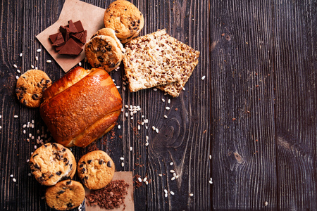 Top view on homemade bun and a variety of cookies on dark rustic wooden table with space for text.の写真素材