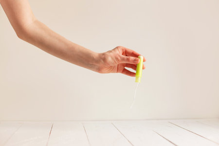 Womans hand holding clean green cotton tampon.