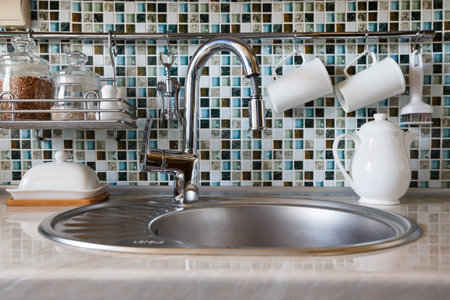 Modern kitchenware and utensils including mugs, cups, tea pot and jars with cereal around tap and...